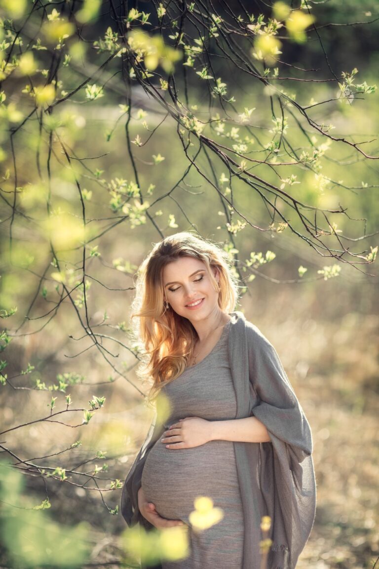 Expectant mother in a grey dress and shawl under budding spring branches