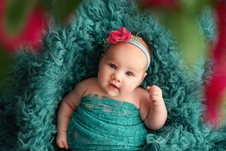 Baby girl in a teal lace wrap and red flower headband on teal fur