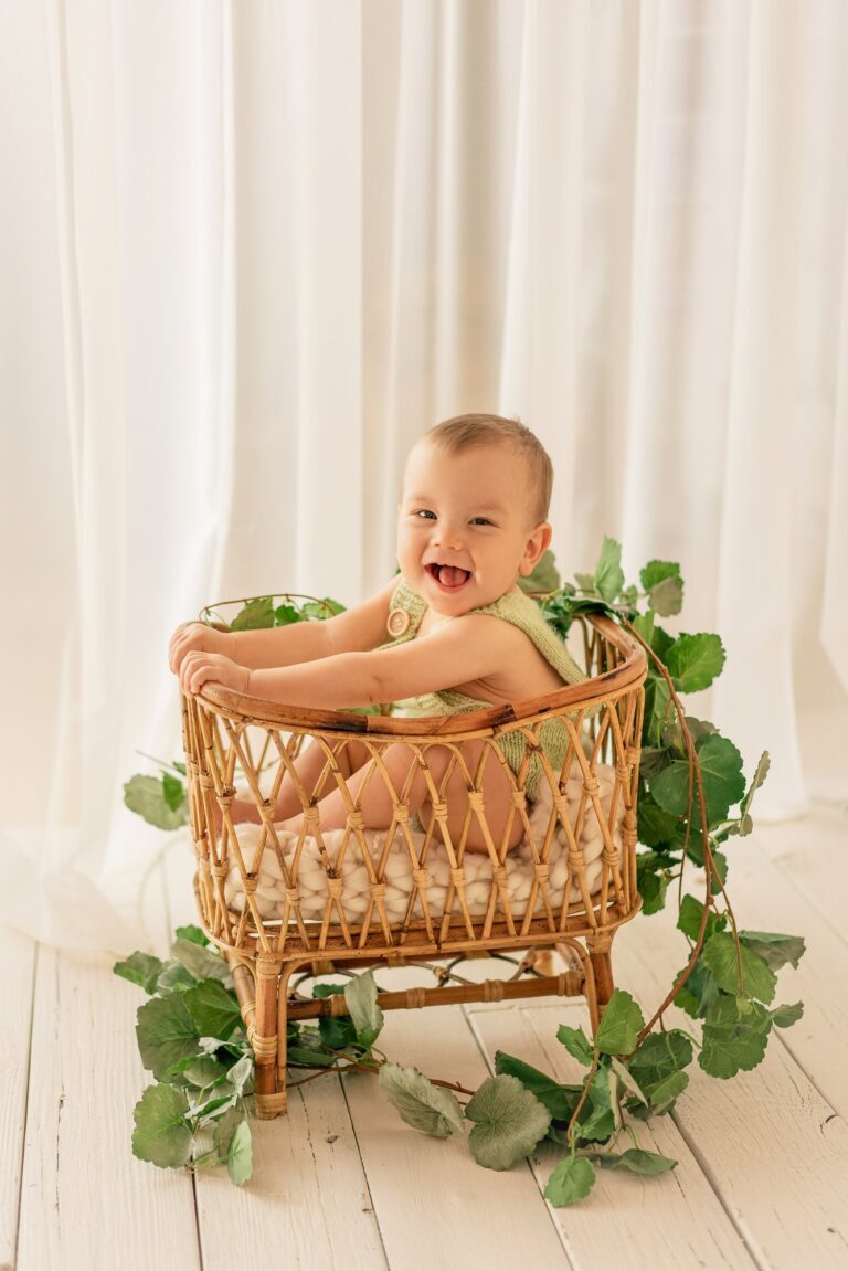 Laughing baby in a rattan crib wrapped in ivy on white floorboards