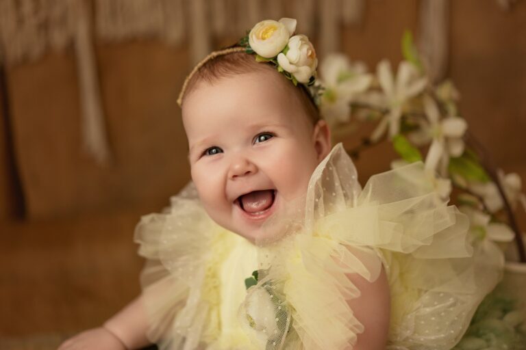 Laughing baby girl in a pale yellow tulle dress and cream rose headband