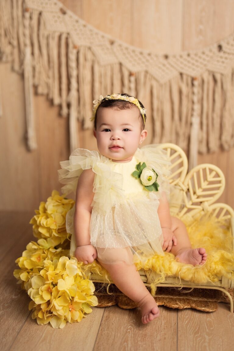 Baby girl in a yellow tulle romper on a rattan bench with yellow hydrangeas