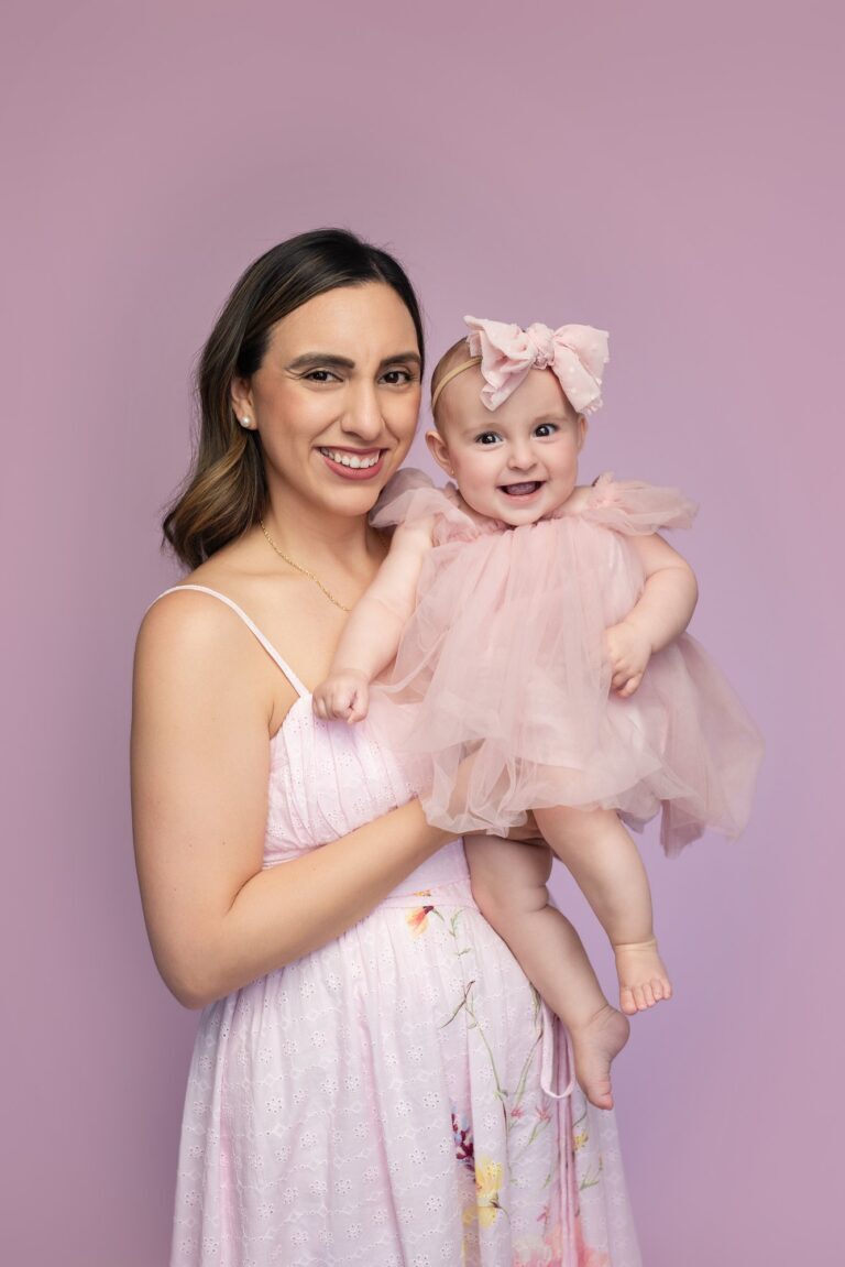 Smiling mother and laughing baby girl in pink tulle against a lilac backdrop