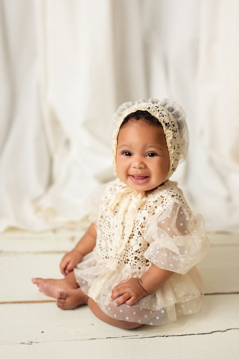 Smiling baby in a cream lace bonnet and polka dot tulle romper