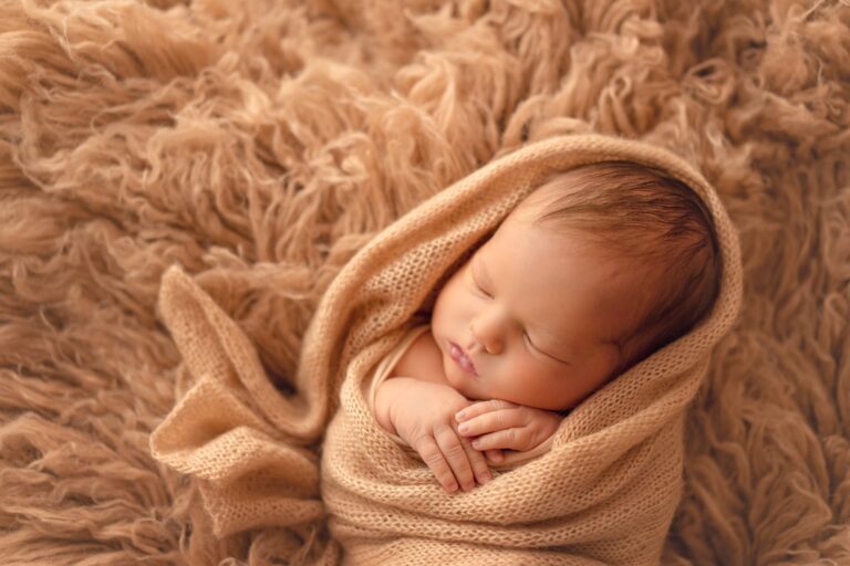 Close-up of a sleeping newborn in a camel knit wrap on caramel fur