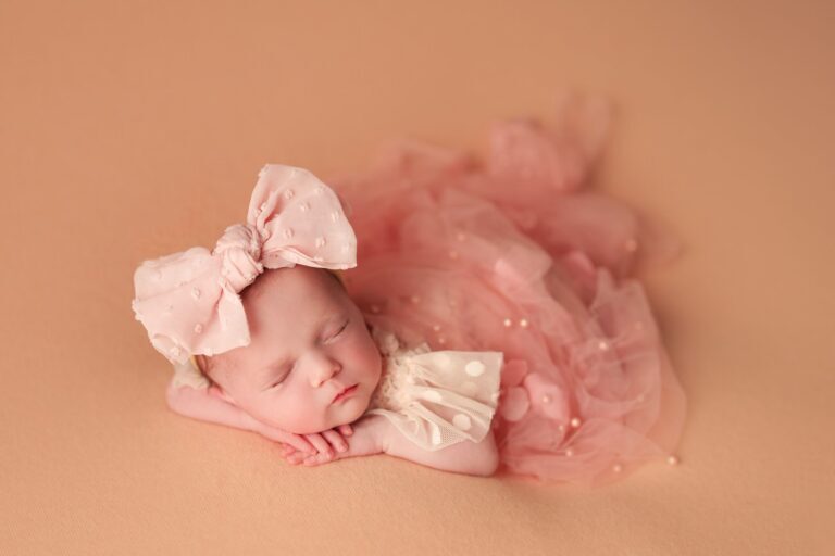 Sleeping newborn in a pink tulle dress and oversized polka dot bow on peach
