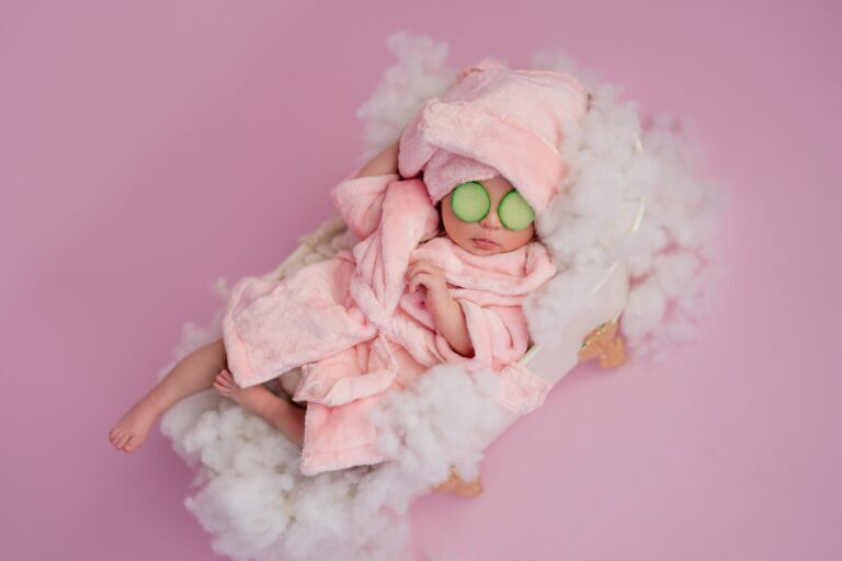Newborn in a pink robe and towel turban with cucumber slices over the eyes