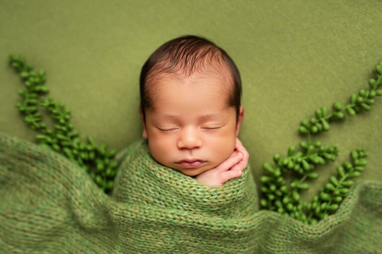 Close-up of a sleeping newborn tucked under a green knit blanket