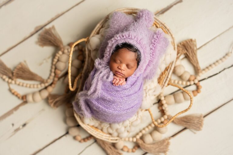 Newborn in a ruffled lilac mohair bonnet and wrap asleep in a woven basket