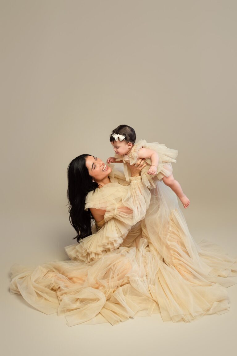 Mother in a flowing cream tulle gown lifting her baby girl overhead