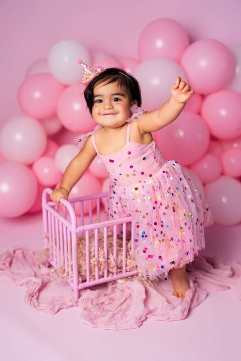 Smiling girl in confetti tulle and a party crown leaning on a pink crib