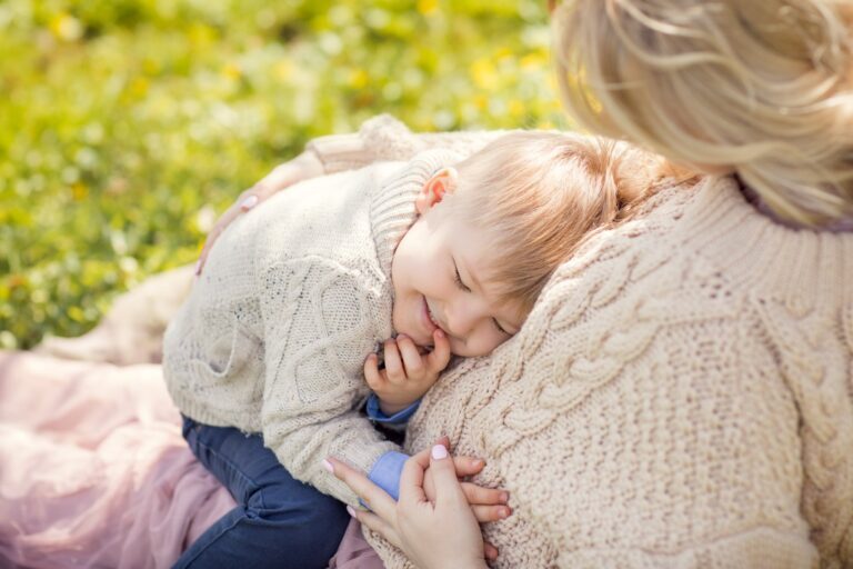 Toddler boy in a cable-knit sweater cuddling his pregnant mother's belly