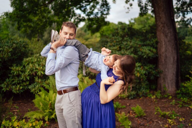 Father swinging his laughing toddler as the mother in a blue lace gown smiles