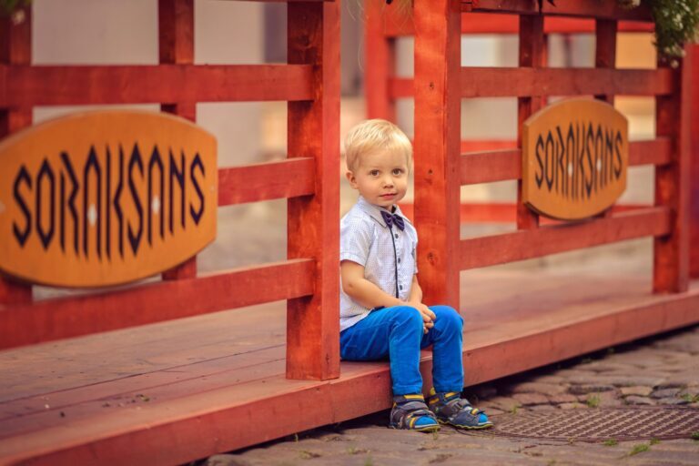 Toddler boy in a bow tie and blue trousers on a red wooden deck