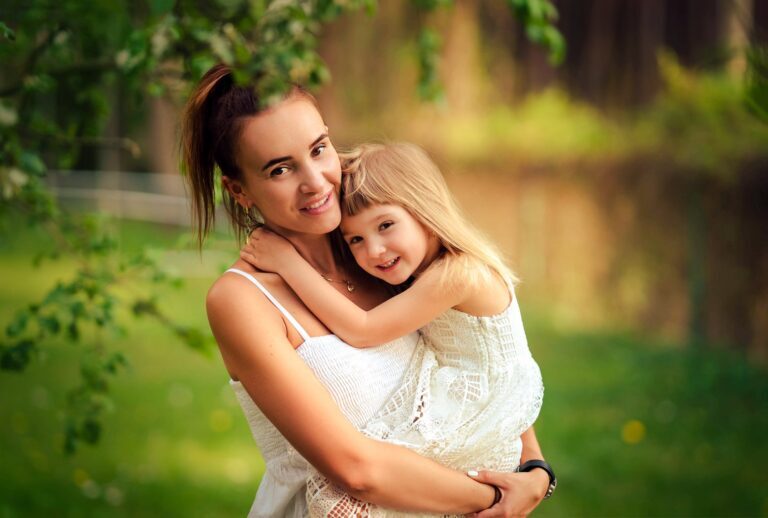 Mother in a white top hugging a smiling girl in a white lace dress