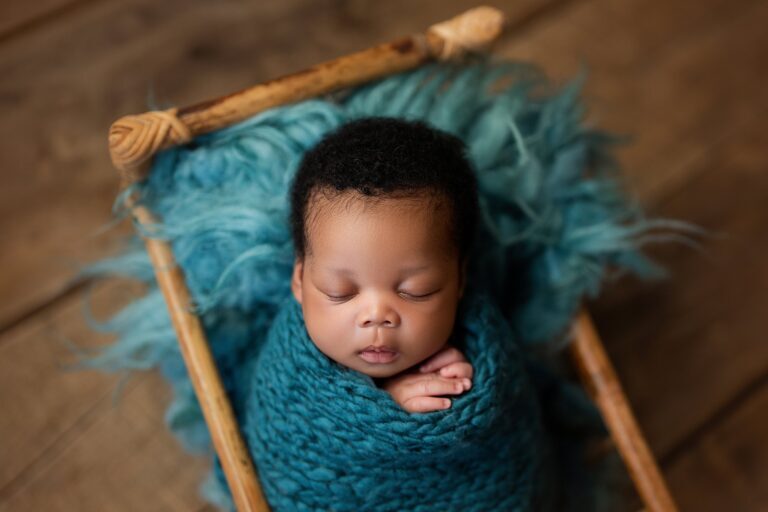 Newborn in a chunky teal knit wrap asleep on teal fur in a wooden bed