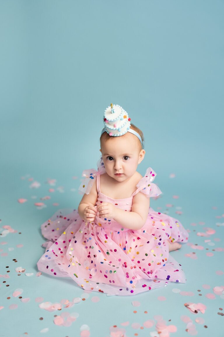 Baby girl in a dotted pink tulle dress and cake-shaped hat on a blue backdrop
